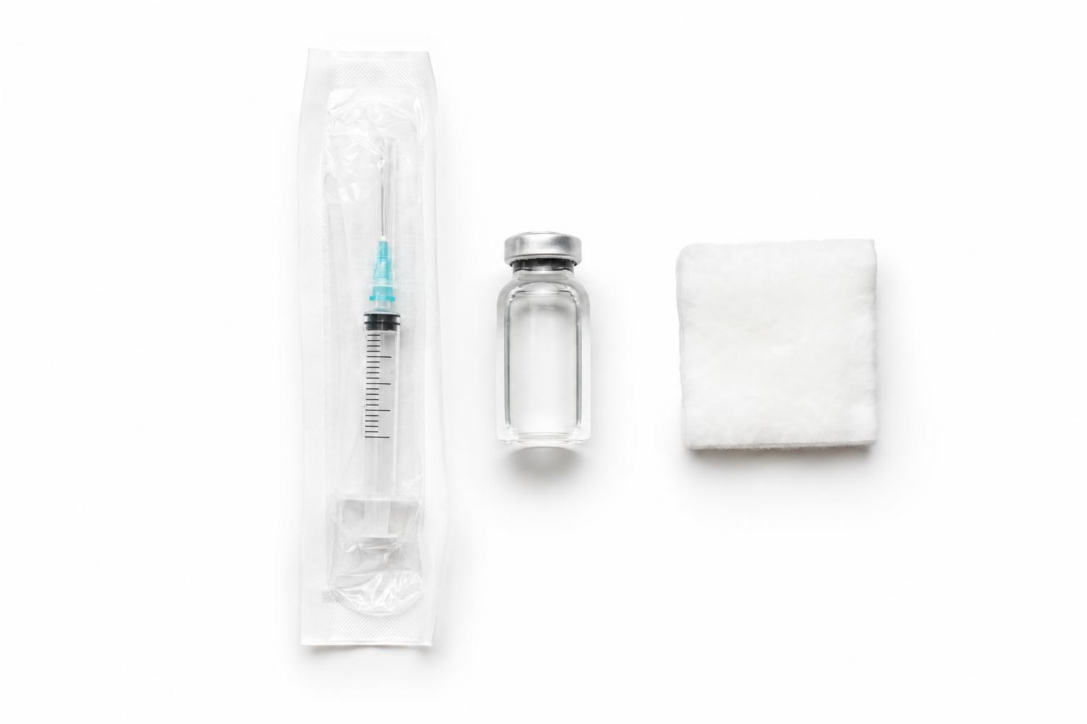 A sealed syringe beside a small vaccine vial and cotton wool